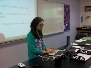 Ms. Amanda Corrado works on her computer at her desk during a presentation in her classroom.