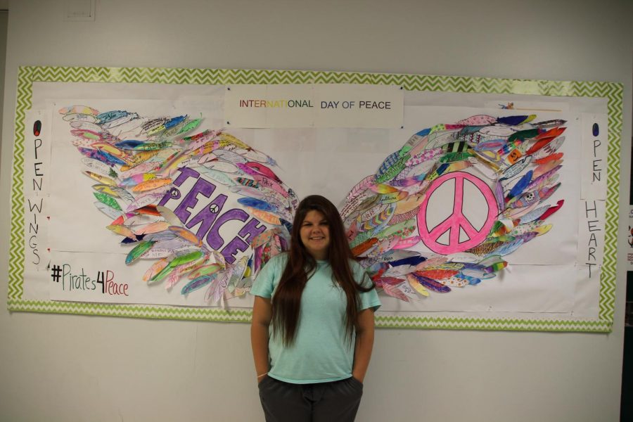 Kelsey+Hendricks+takes+a+photo+in+front+of+the+International+Clubs+interactive+peace+wings+mural.+