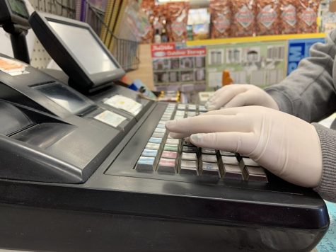 Cashier Megan Weeks wears protective gloves to help protect herself and the customers from the COVID-19 while she checks people out at Branneky Hardware. 
